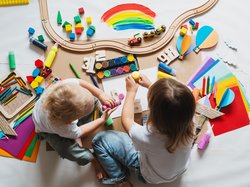 Zwei Vorschulkinder sitzen auf einem großen Stück Papier, malen und basteln