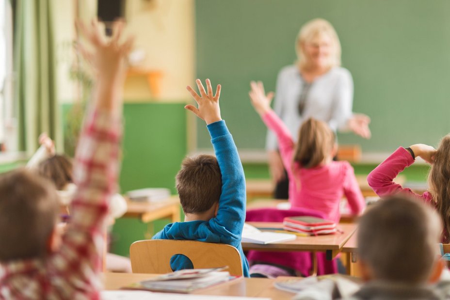 Grundschulkinder heben eifrig die Hände, um die Frage ihrer Lehrerin zu beantworten 