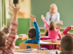 Grundschulkinder heben eifrig die Hände, um die Frage ihrer Lehrerin zu beantworten 